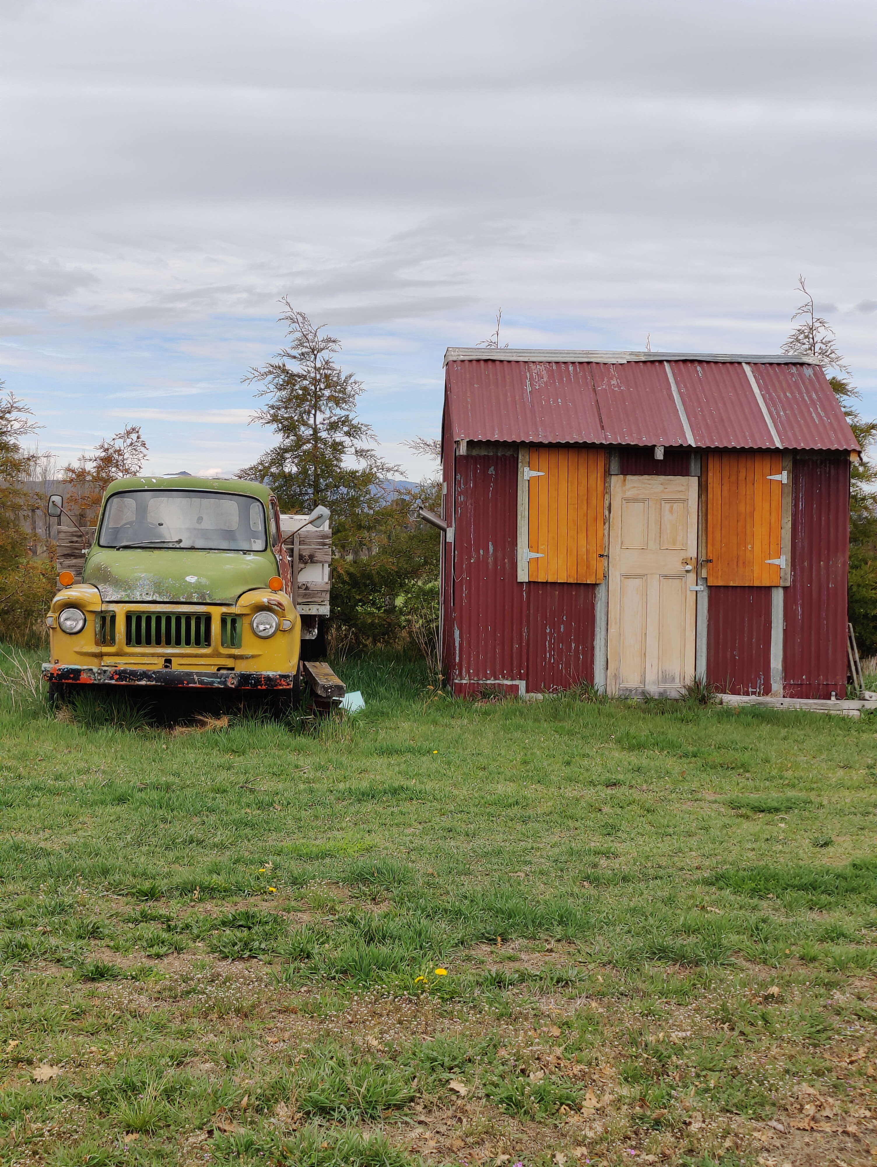 Old green truck beside a red rural shed